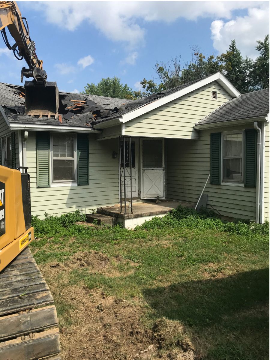 Mini excavator trenching a rock drain line across a yard